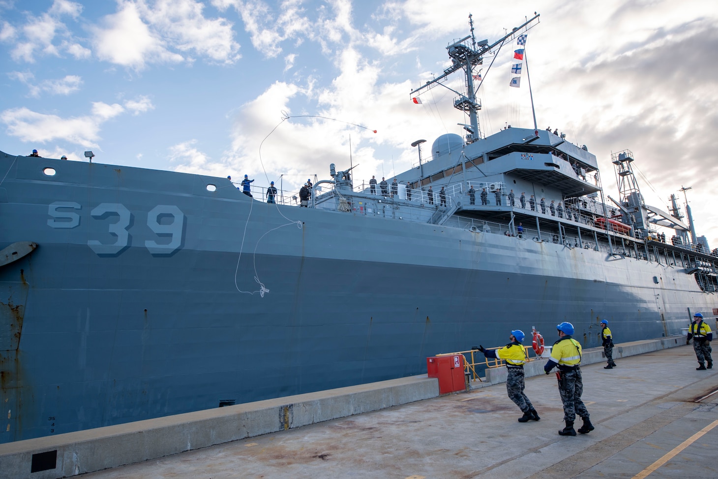 Military Sealift Command civil service mariners assigned to the submarine tender USS Emory S. Land (AS 39) throw a heaving line from the ship to Royal Australian Navy sailors on the pier as the Emory S. Land moors at HMAS Stirling, Western Australia, Australia, Aug. 16.