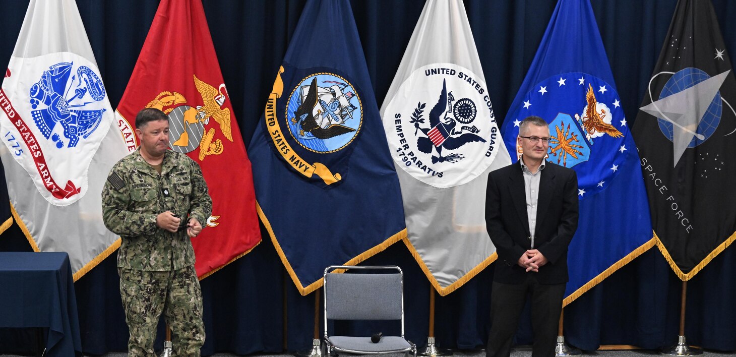 DAHLGREN, Va. (July 08, 2024) Cmdr. Jonathan Schermerhorn, commanding officer, Surface Combat Systems Training Command AEGIS Training and Readiness Center (SCSTC ATRC), discusses Mr. Jeff Noordyk’s, SCSTC ATRC’s director of Training, contributions to the schoolhouse and the Aegis community during a farewell event onboard Naval Support Facility Dahlgren, Virginia.  (U.S. Navy photo by Michael Bova)